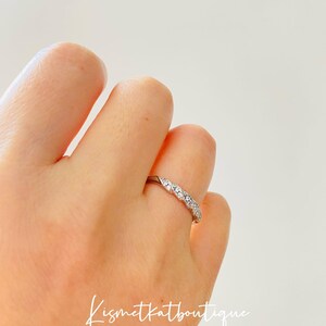 Op de afbeelding: Een zilveren ring met een rij kleine, heldere edelstenen in een herhalend patroon. De ring zit om een vinger, met de tekst "Kismetkatboutique" in cursief.