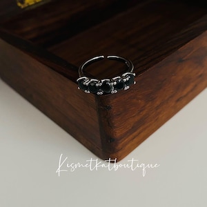 May include: A silver ring with five black gemstones set in a row. The ring is in a wooden box.