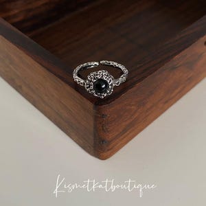 May include: A silver ring with a black stone set in a floral design.