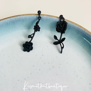 May include: A pair of black rose earrings with a delicate stem design. The earrings are made of metal and have a matte finish.