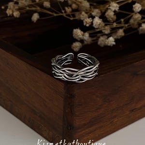 May include: A silver-colored ring with a woven design. The ring is open at the top and sits on a wooden surface. The Etsy shop name "Kismetkatboutique" is visible at the bottom of the image.