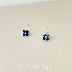Puede incluir: Un par de pendientes de plata con un diseño de flor azul. Cada pendiente tiene cuatro piedras azules y una sola piedra transparente en el centro.