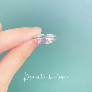 May include: A silver toe ring with a fish design. The ring is adjustable and can be worn on any toe.