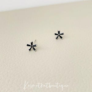 May include: A pair of silver stud earrings with black star-shaped accents.