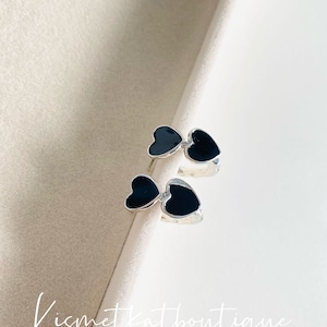 May include: A pair of silver hoop earrings with black enamel hearts. The hearts are connected to each other and the hoops are open.