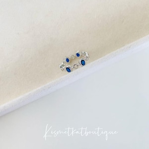 May include: A silver ring with a chain design and blue oval-shaped stones.