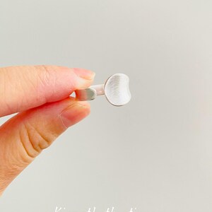May include: A silver-toned ring featuring a flat, circular disc face with a brushed, matte texture. The band is open at the back, allowing for adjustment. The text Kismetkatboutique is printed in white at the bottom of the image frame.