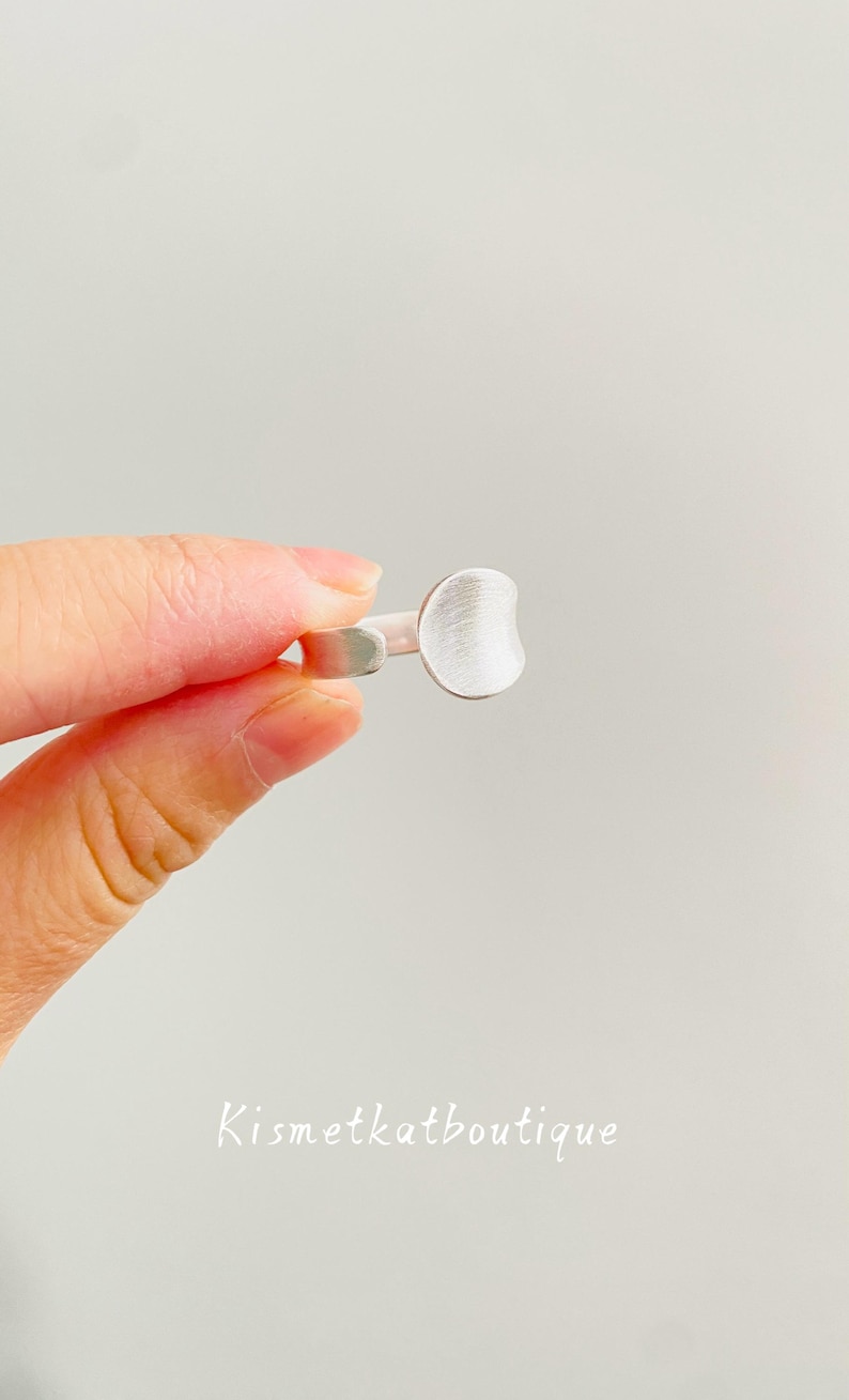 May include: A silver-toned ring featuring a flat, circular disc face with a brushed, matte texture. The band is open at the back, allowing for adjustment. The text Kismetkatboutique is printed in white at the bottom of the image frame.
