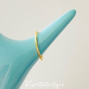 May include: A simple gold band ring on a blue display stand.