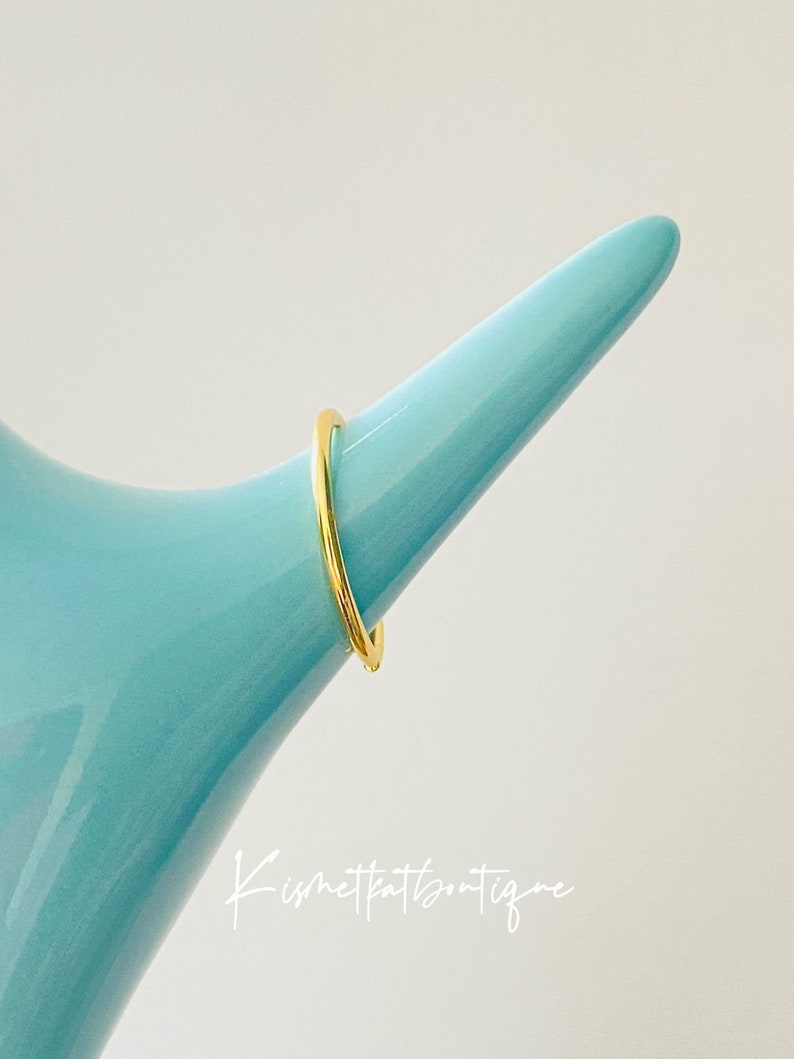 May include: A simple gold band ring on a blue display stand.