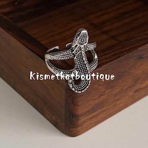 May include: A silver-toned metal ring shaped like a coiled snake with a textured, dotted surface pattern. The ring features an open-band design and includes the text Kismetkatboutique overlaid across the center of the snake figure.
