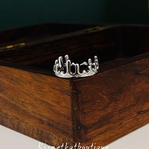 Op de afbeelding: Een zilverkleurige ring met een uniek, gesmolten ontwerp. De ring ligt op een houten kistje met een donkergroene achtergrond. De winkelnaam "Kismetkatboutique" is zichtbaar.