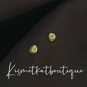Könnte beinhalten: Ein Paar kleine, runde, grüne Ohrringe. Die Ohrringe befinden sich auf einem schwarzen Stoffhintergrund. Der Text "Kismetkatboutique" ist in der rechten unteren Ecke des Bildes sichtbar.