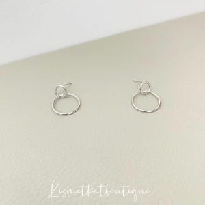 May include: A pair of silver hoop earrings with a smaller circle hanging from the larger circle.