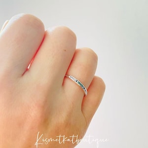 May include: A silver ring with a delicate design on the band. The ring is worn on a person's finger.