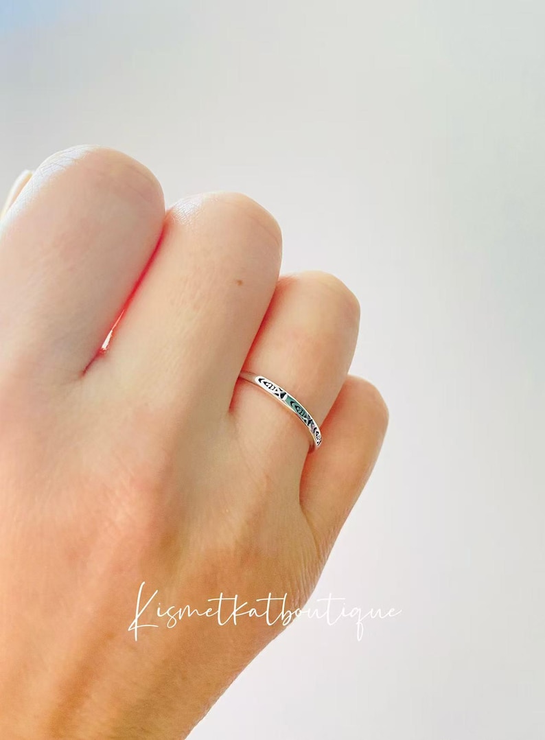 May include: A silver ring with a delicate design on the band. The ring is worn on a person's finger.
