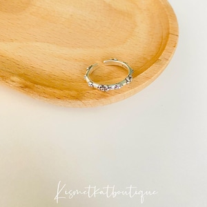 Puede incluir: Un anillo de plata con un delicado diseño floral. El anillo es ajustable y tiene un estilo simple y elegante.