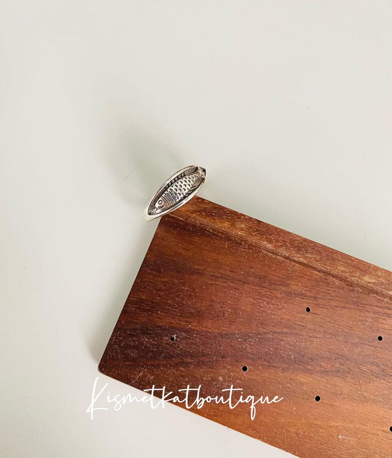 May include: Silver ring with a detailed fish design. The ring is on a wooden surface with the text "Kismetkatboutique" visible.
