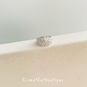 May include: A silver-toned adjustable ring with a textured surface, adorned with small, sparkling embellishments. The ring is displayed on a neutral-toned surface. The text "Kismetkatboutique" is visible.