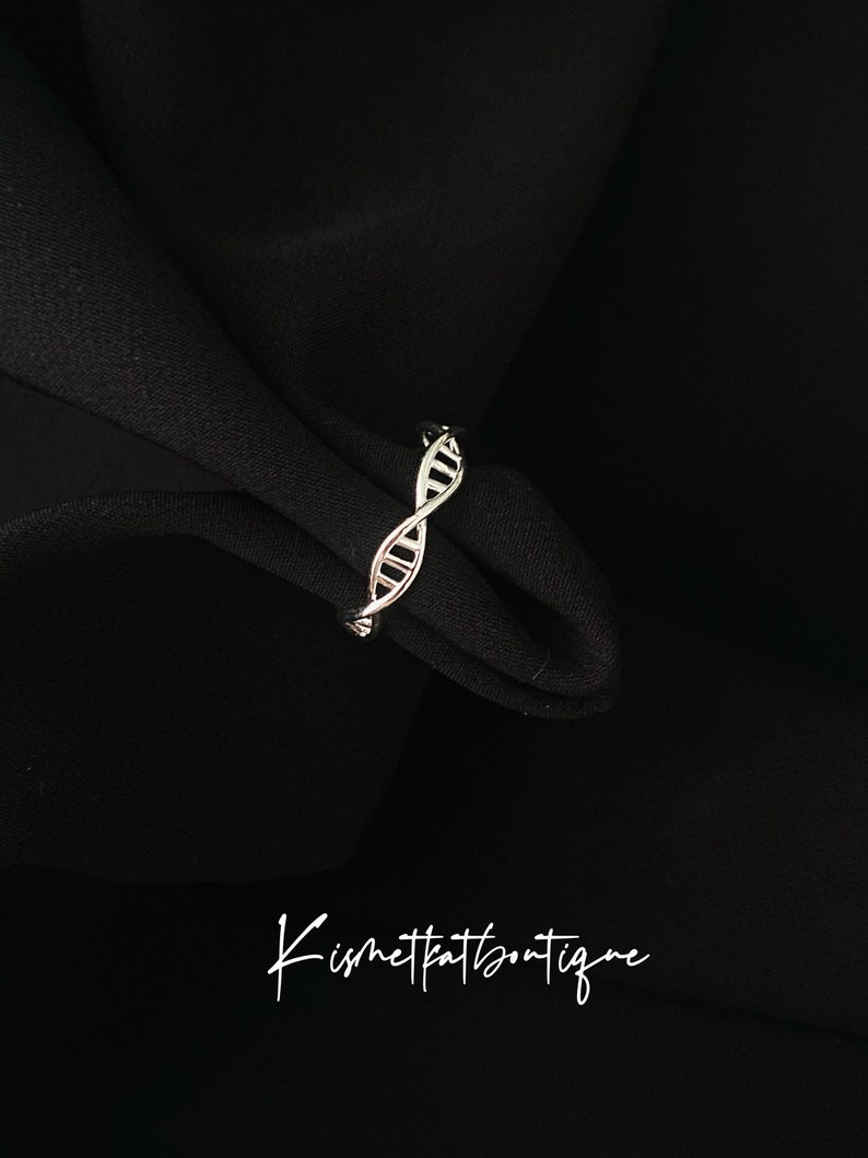May include: A silver ring, designed as a DNA double helix, set against a black backdrop. The image includes the cursive text "Kismetkatboutique" at the bottom.