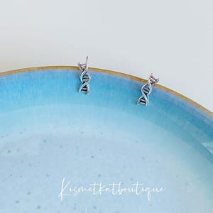 May include: A pair of silver DNA helix hoop earrings on a light blue plate. The earrings are small and delicate.
