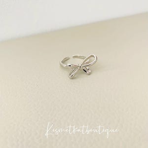 Può includere: Un anello d'argento con un design a fiocco. L'anello è semplice ed elegante.