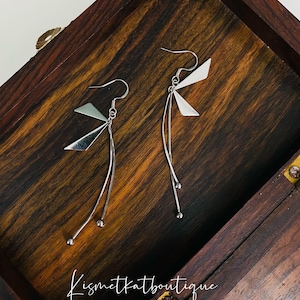 May include: A pair of silver dangle earrings with a geometric design. The earrings feature a triangular shape with a small ball at the end of each dangle.