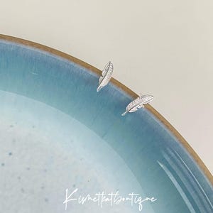 May include: A pair of silver feather earrings. The earrings are small and delicate, and they are perfect for adding a touch of elegance to any outfit.