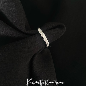 Op de afbeelding: Een zilveren ring met een doorlopende rij kleine, sprankelende stenen. De ring is geplaatst tegen een zwarte stoffen achtergrond. De tekst "Kismetkatboutique" staat in cursief onderaan de afbeelding.