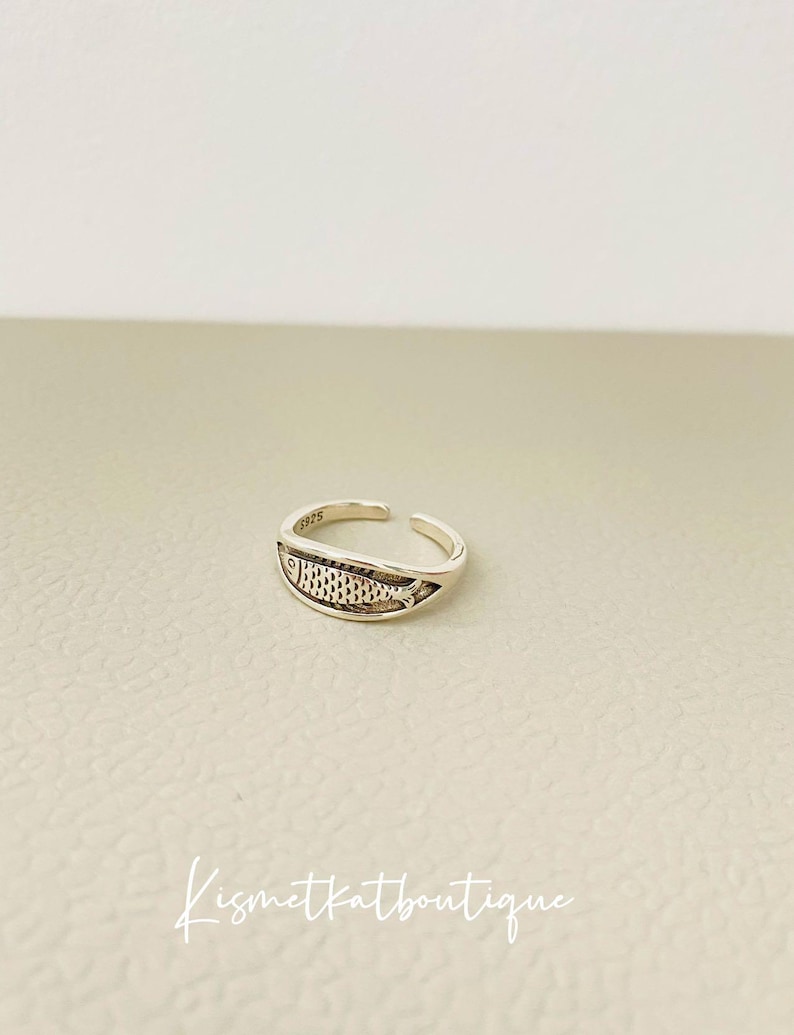 May include: Silver adjustable ring with a detailed fish design. The ring is marked with the number "925".