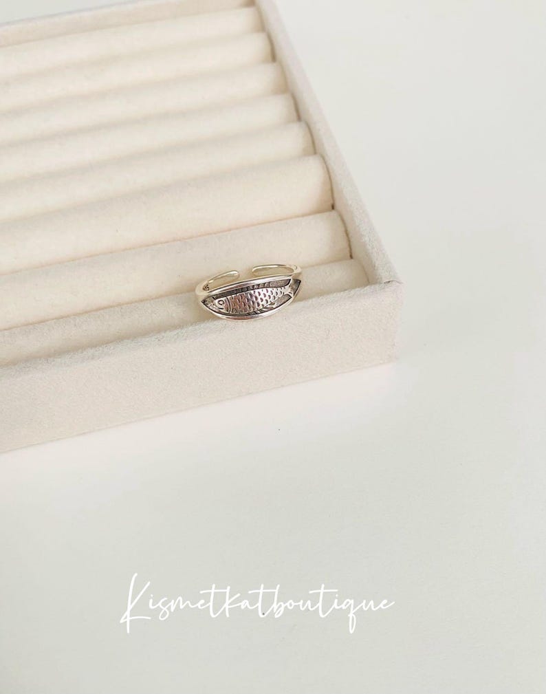 May include: A silver adjustable ring with a fish design. The ring is on a white background.