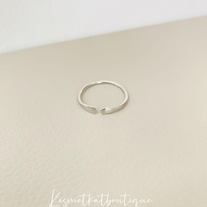 May include: A simple silver ring with a slightly open design. The ring is smooth and has a subtle shine.