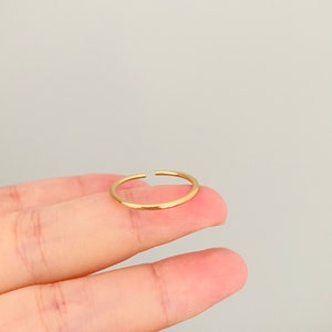 May include: A simple gold ring with a smooth, rounded surface. The ring is open on one side, making it adjustable to fit different finger sizes.