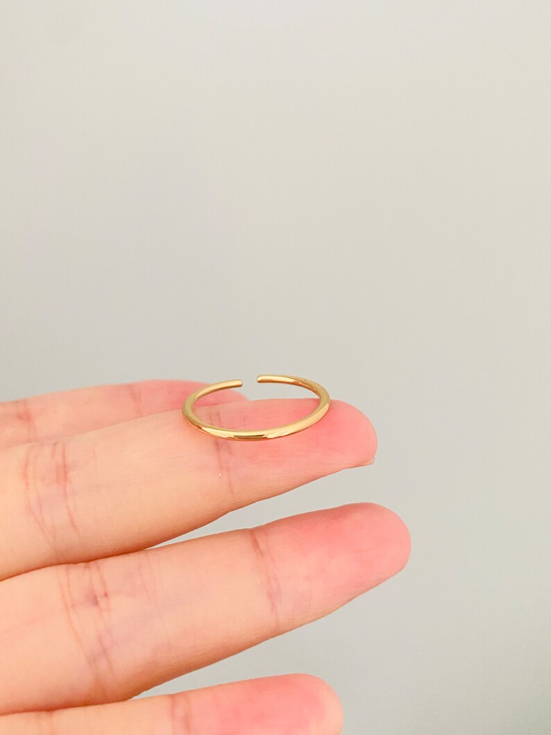 May include: A simple gold ring with a smooth, rounded surface. The ring is open on one side, making it adjustable to fit different finger sizes.