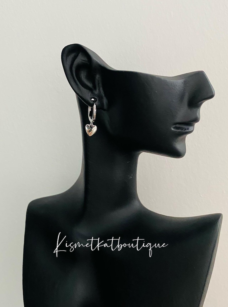 May include: Silver hoop earrings with a small heart charm dangling from each hoop.