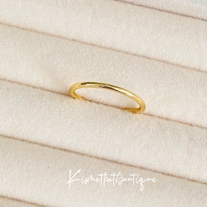 May include: A simple gold band ring on a white velvet background.