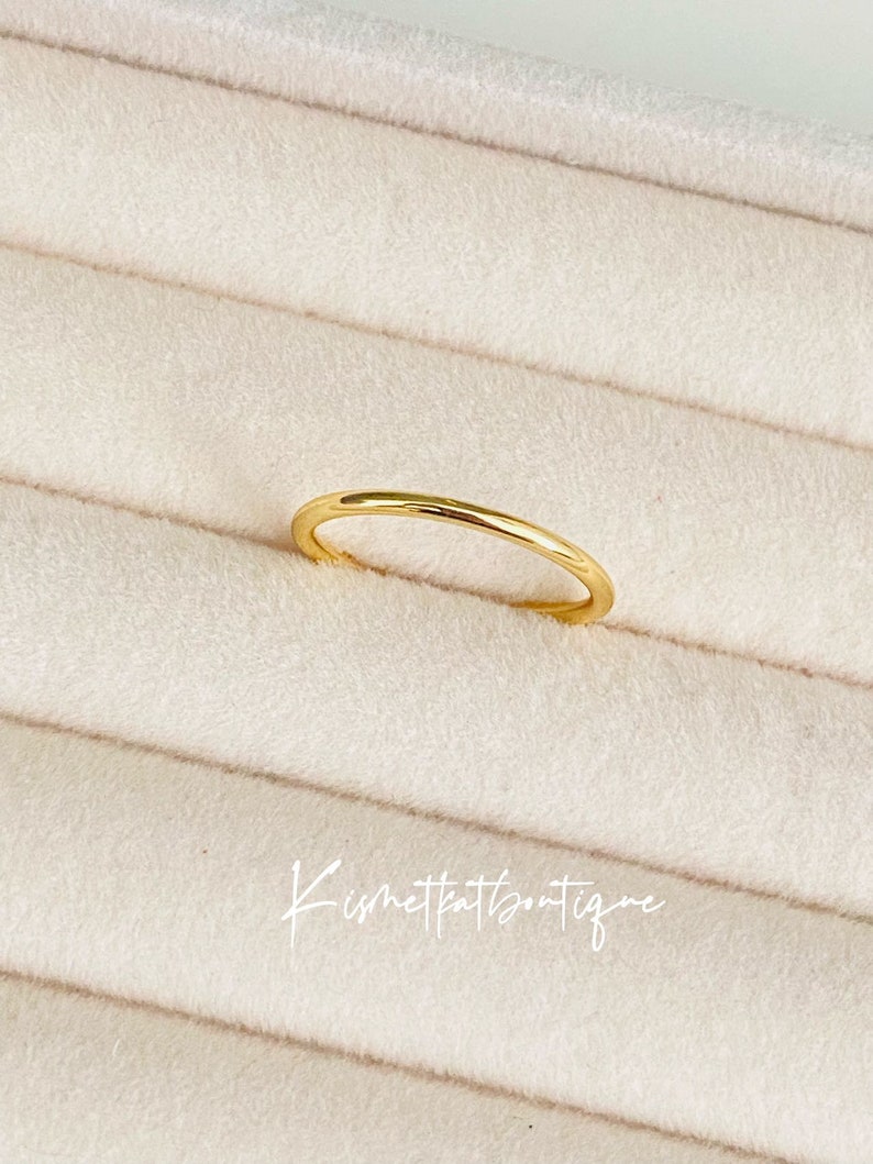 May include: A simple gold band ring on a white velvet background.