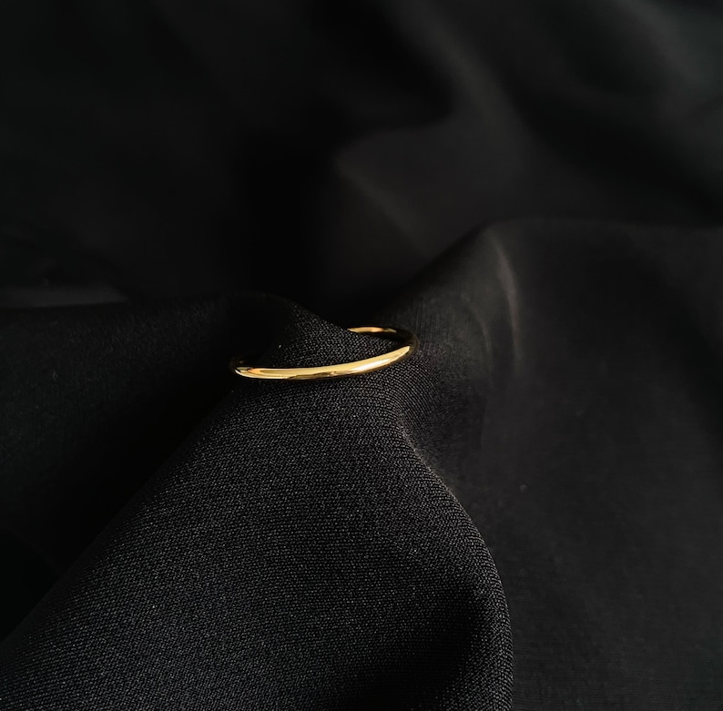 May include: A simple gold band ring, lying on a black fabric background.