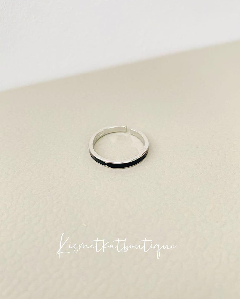 Pu&ograve; includere: Un anello d'argento con una sottile fascia nera attorno al centro.