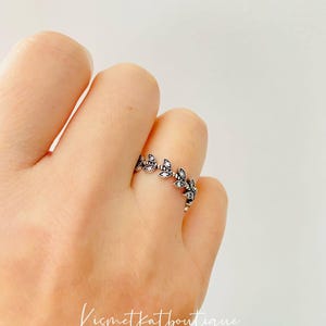 Puede incluir: Un anillo de plata con un delicado diseño de hojas y pequeñas piedras transparentes. El anillo está en un dedo.