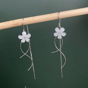 May include: A pair of silver dangle earrings with white flower charms. The earrings have a delicate, twisted design.