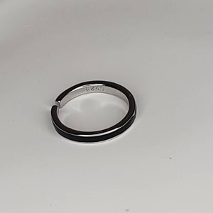 Pu&ograve; includere: Un anello d'argento con una fascia nera attorno al centro. L'anello ha il numero "6243" inciso all'interno.