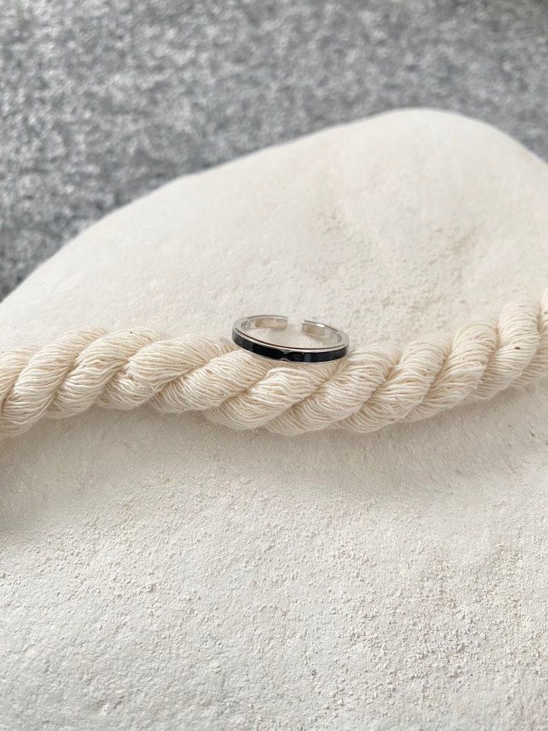 Pu&ograve; includere: Un anello d'argento con una fascia nera attorno al centro.