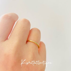 May include: A simple gold band ring worn on a finger.