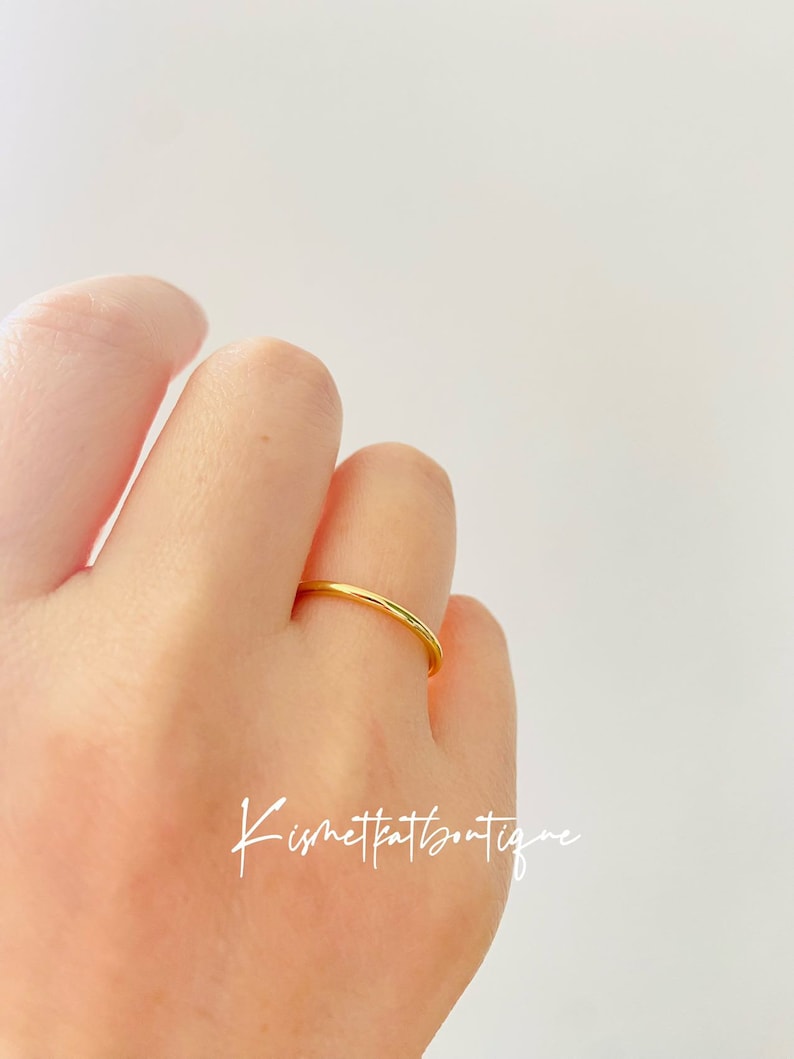 May include: A simple gold band ring worn on a finger.