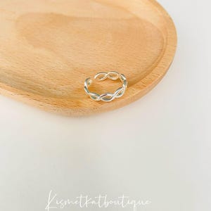 May include: Silver braided adjustable ring. The ring is made of a thin, braided metal and is designed to fit a variety of finger sizes.