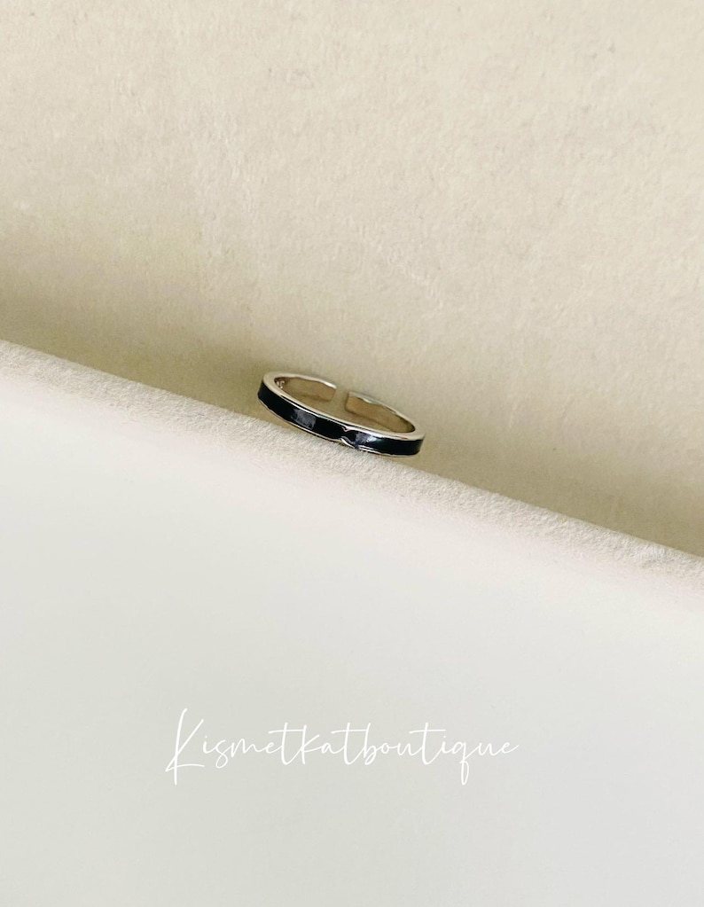 Pu&ograve; includere: Un anello d'argento con una fascia in smalto nero. L'anello &egrave; aperto e regolabile.