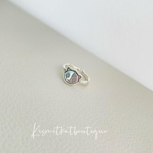 May include: A silver-toned ring with a cat-shaped face design. The cat's face features a colorful, iridescent pattern. The ring is on a light-colored surface. The text "kismetkatboutique" is written in cursive.