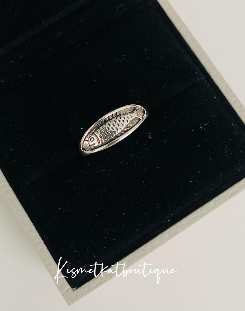 May include: A silver ring with a detailed fish design. The ring is displayed in a black velvet box with a white border and the text "Kismetkatboutique".