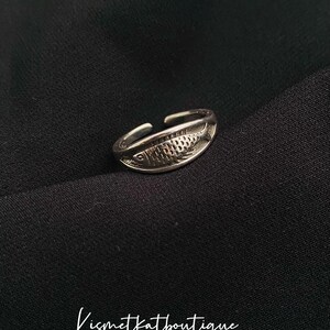 May include: A silver adjustable ring with a fish design. The fish is detailed with scales and has a slightly curved shape.